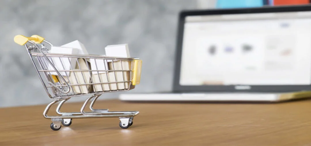 Tienda online: carrito de compras en una mesa con computador de fondo